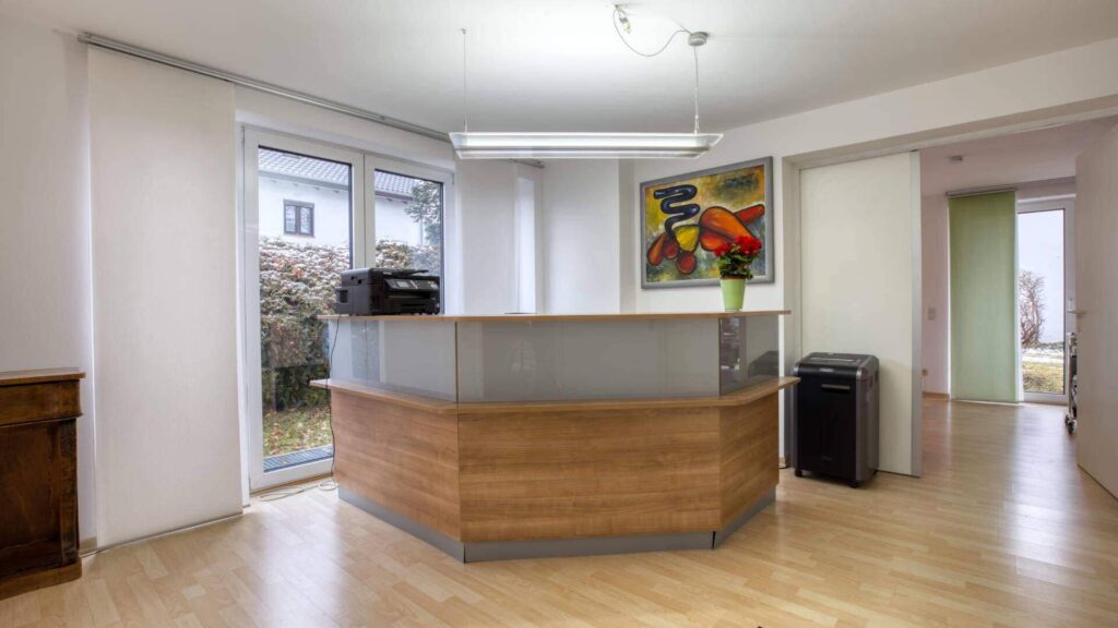 Empfangstheke aus Holz und Glas mit buntem Wandbild im Büroeingang in München-Forstenried
