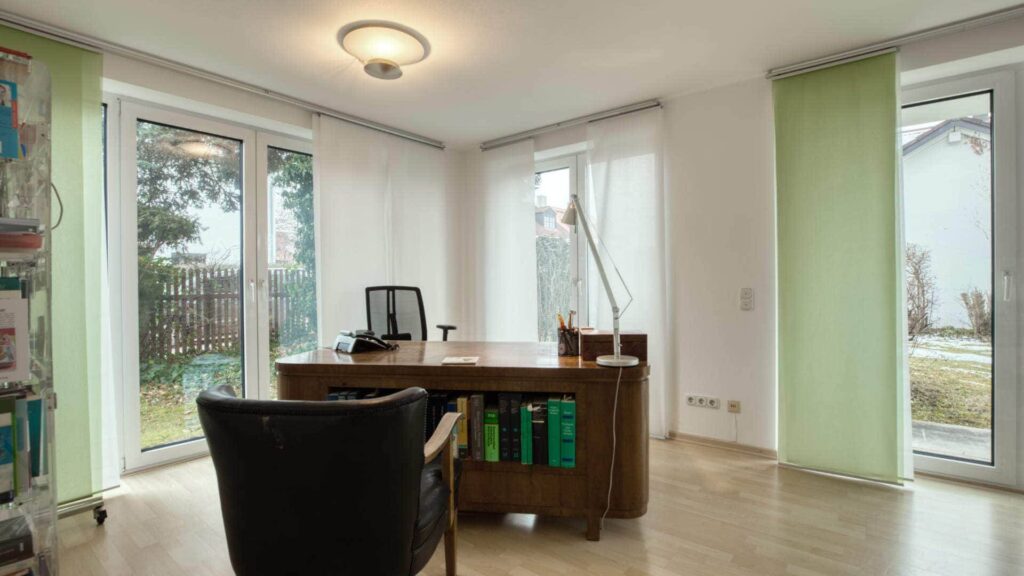 Büroraum mit Schreibtisch, Ledersessel und großen Fenstern zur Terrasse in München-Forstenried
