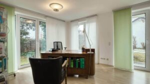 Office space with a desk, leather armchair, and large windows leading to the patio in Munich-Forstenried
