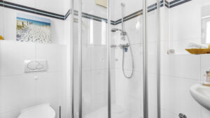 Badezimmer mit Eckdusche, WC und weißen Fliesen unter der Dachschräge in einer Wohnung in München-Forstenried