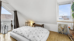 Schlafzimmer mit Bett unter der Dachschräge und Balkonzugang in einer Wohnung in München-Forstenried
