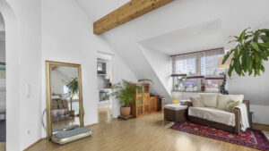 Living room with exposed wooden beams under the sloped ceiling and a light-colored sofa in an attic apartment in Munich-Forstenried