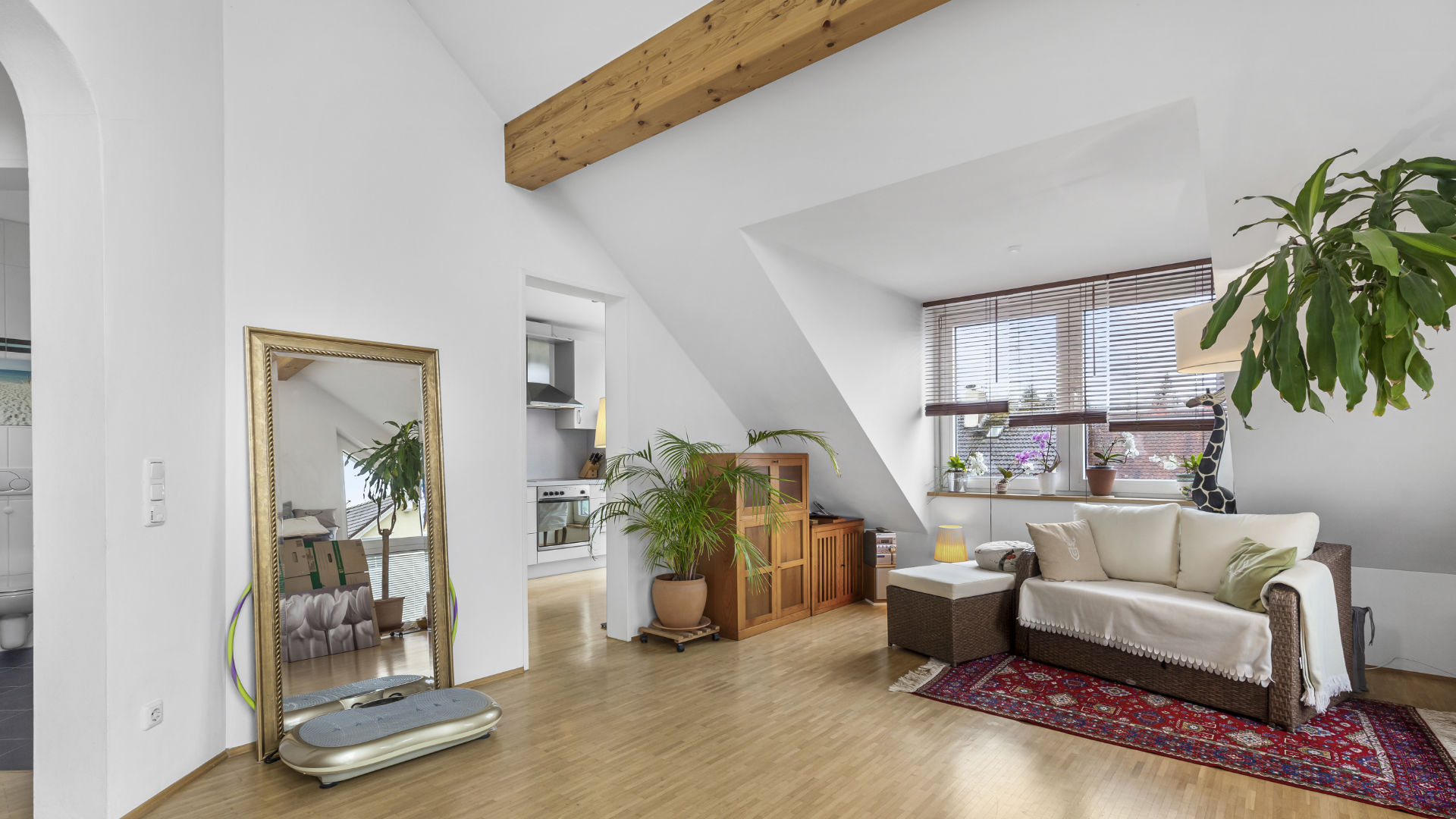 Living room with exposed wooden beams under the sloped ceiling and a light-colored sofa in an attic apartment in Munich-Forstenried