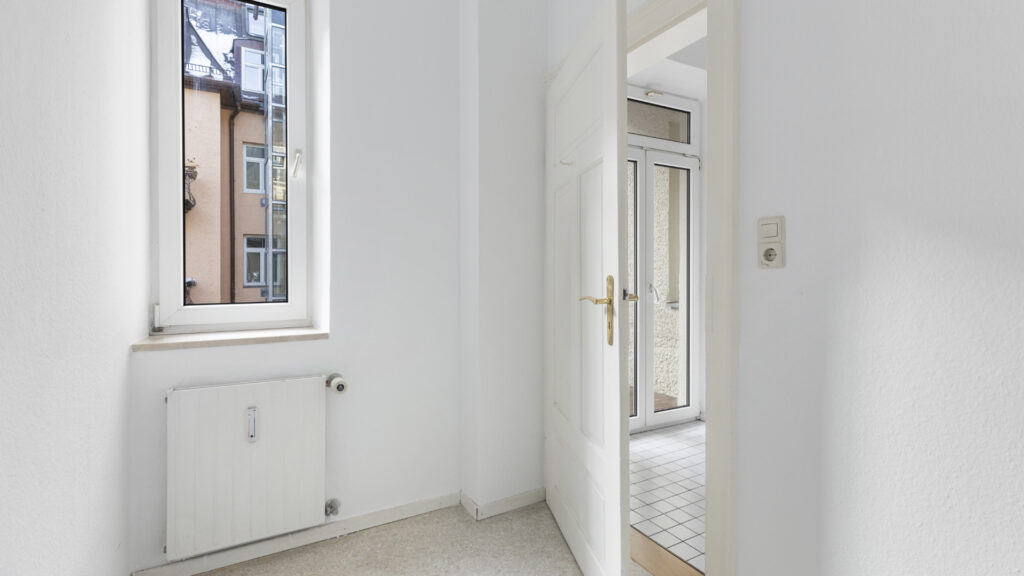Small, unfurnished room with a window and a radiator in an older apartment in Munich's Gärtnerplatz neighborhood