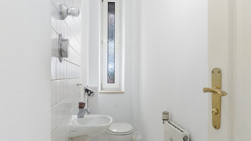 Small guest toilet with washbasin, window, and gold door handle in an old building apartment in the Gärtnerplatzviertel in Munich