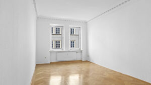 Unfurnished living room with two vintage windows and glossy hardwood floors in Munich’s Gärtnerplatz neighborhood