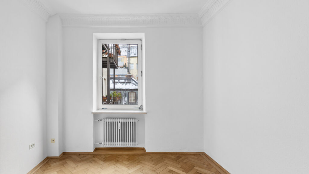 Unfurnished room with herringbone parquet flooring, vintage windows, and radiators in an apartment in Munich's Gärtnerplatz district