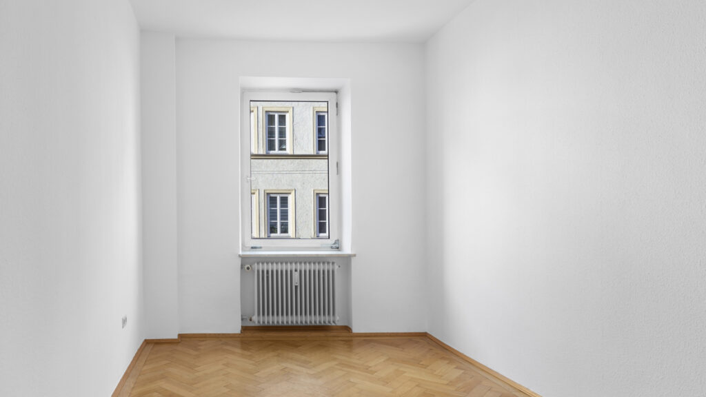 Unfurnished room with a high old-building window, radiator, and parquet flooring in an apartment in the Gärtnerplatzviertel district of Munich