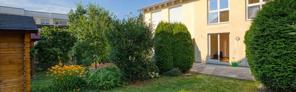 Gepflegter Garten des Hauses in Germering mit Rasenfläche, Hecken, Blumenbeet und Gartenhaus