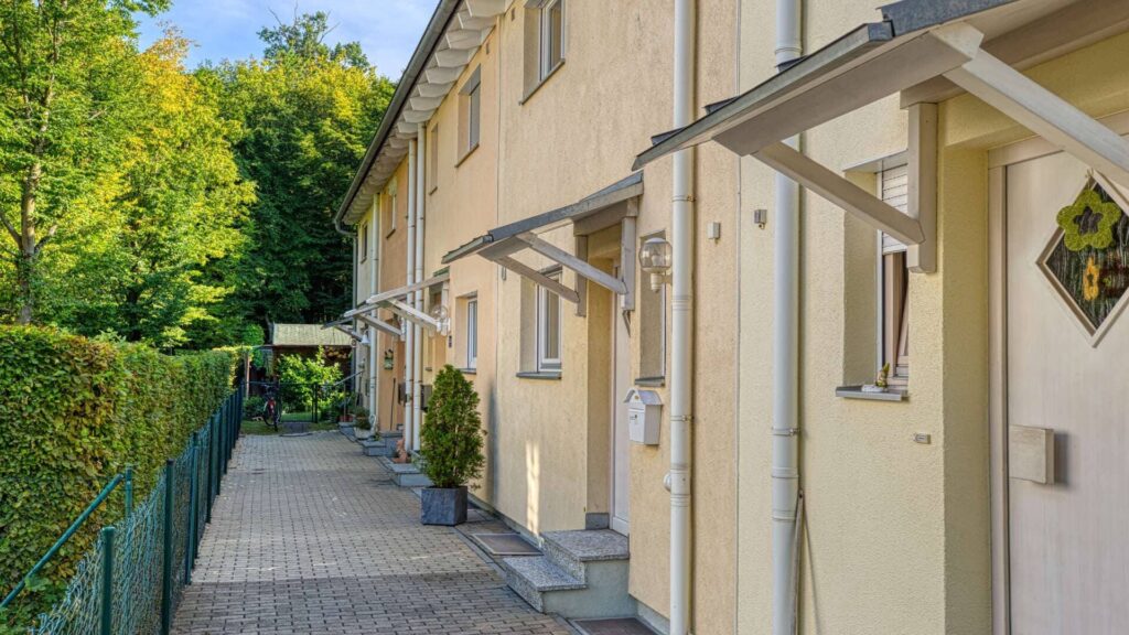 Gepflasterter Zugangsweg zum Reihenhaus in Germering mit Hecke, Vordach und Eingangstüren