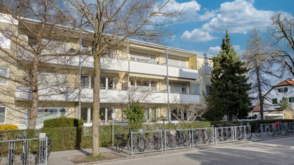 Apartment building with bicycle stands and a fence by the street in Germering – Rogers Immobilien