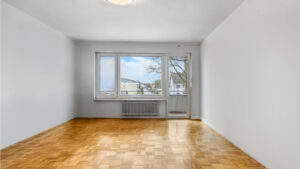 Empty living room with parquet flooring and balcony access in the apartment Germering – Rogers Immobilien