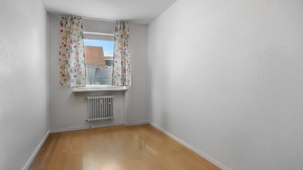 Empty room with floral curtains and wooden floor in the Germering apartment – Rogers Immobilien