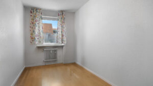 Empty room with floral curtains and wooden floor in the Germering apartment – Rogers Immobilien