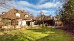 Gartenansicht des unsanierten Einfamilienhauses in München-Großhadern mit Rasenfläche und Sträuchern