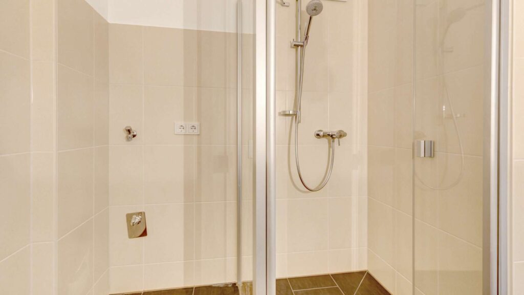 Shower area in the apartment in Munich-Großhadern with glass partition and beige tiles