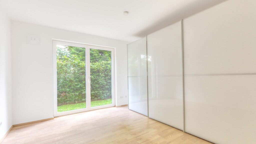 Empty room in the apartment in Munich-Großhadern with a white wall behind the cabinet and a patio door