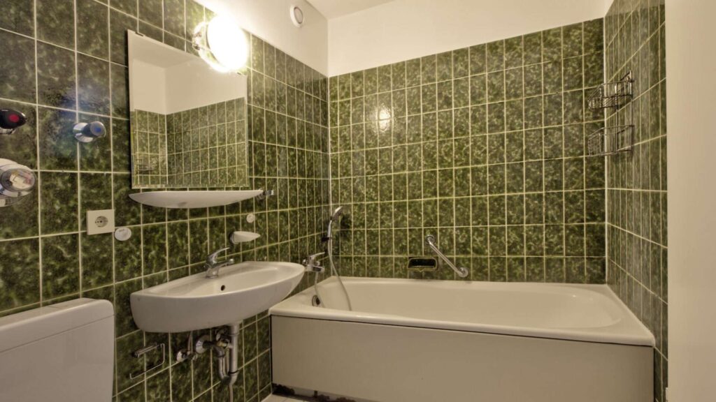Älteres Badezimmer mit grün gefliesten Wänden, Badewanne und Waschbecken in einer Wohnung in München-Hadern