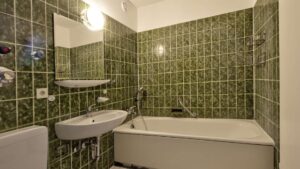 Älteres Badezimmer mit grün gefliesten Wänden, Badewanne und Waschbecken in einer Wohnung in München-Hadern