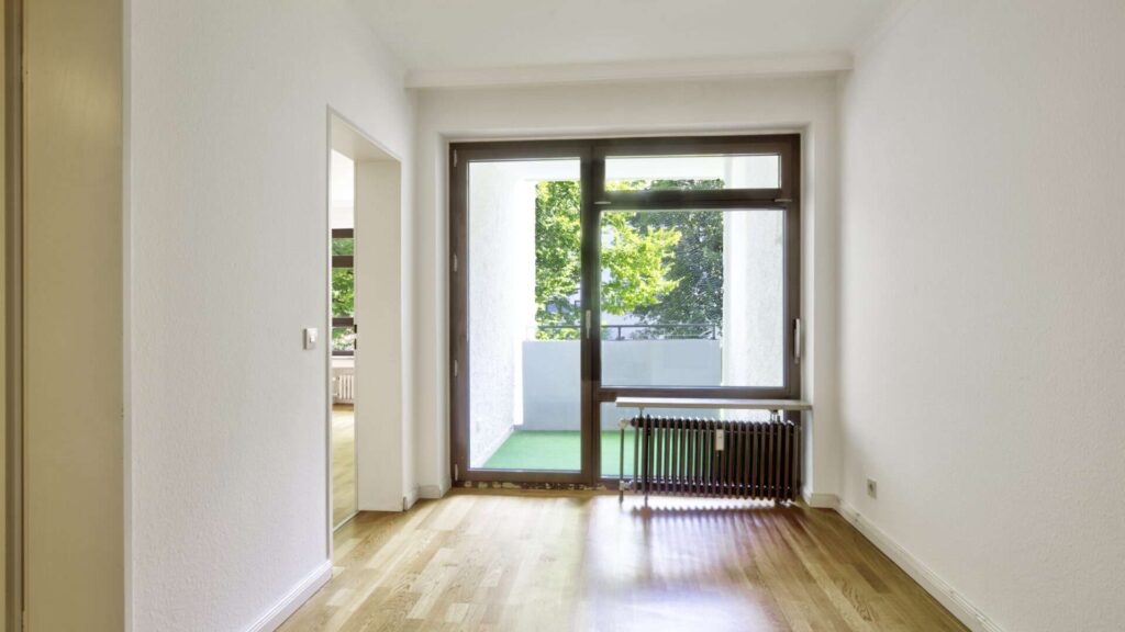 Unmöbliertes Zimmer mit Parkettboden und Terrassentür mit Blick ins Grüne in einer Wohnung in München-Hadern