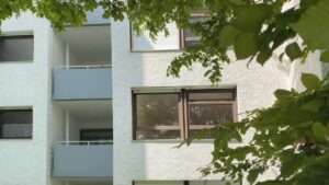 Nahaufnahme der weißen Fassade mit Balkonen und Laubbäumen eines Wohngebäudes in München-Hadern