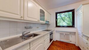 Weiße Einbauküche mit Spüle, Herd und Fenster mit Blick ins Grüne in einer Wohnung in München-Hadern