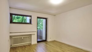 Unmöbliertes Zimmer mit Parkettboden, Heizkörper und Balkontür in einer Wohnung in München-Hadern