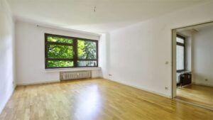 Unmöbliertes Wohnzimmer mit Parkettboden, Fenster und Durchgang zum Nebenraum in einer Wohnung in München-Hadern