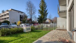 Well-maintained lawn with air conditioning units next to a new residential complex in Herrsching