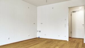 Unfurnished room with parquet flooring and entrance door, intended as a kitchen area in a new-build apartment in Herrsching