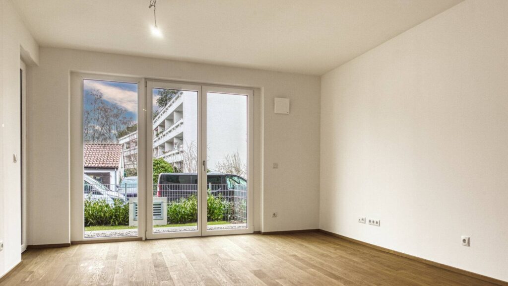 Empty living room with patio door and view of neighboring building in a new construction apartment in Herrsching