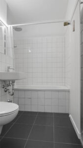 Bathroom with showerhead over the bathtub and white tiles in an apartment in Munich-Laim