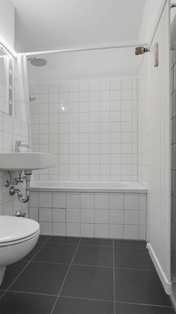 Bathroom with showerhead over the bathtub and white tiles in an apartment in Munich-Laim