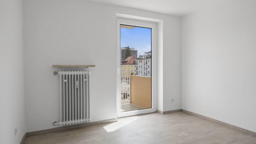 Unfurnished bedroom with radiator, balcony door, and city view in an apartment in Munich-Laim