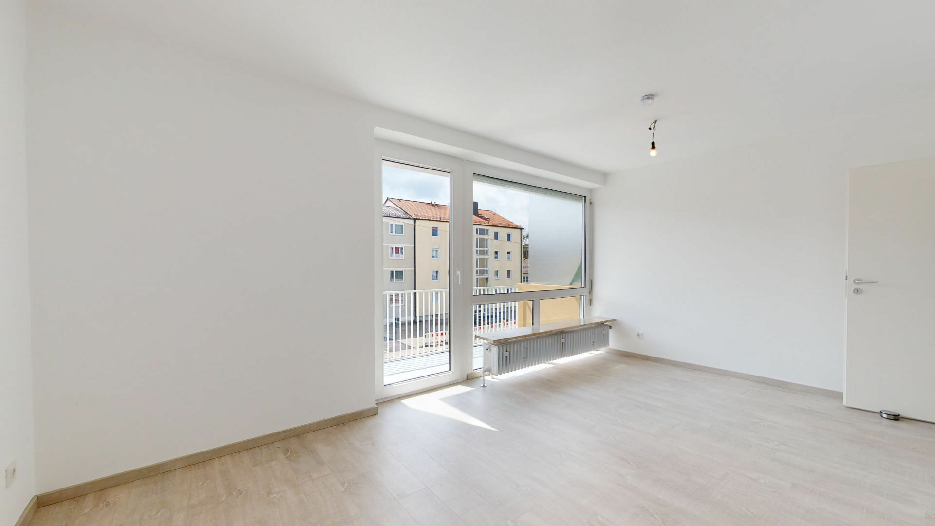 Unfurnished living room with light flooring, balcony door, and city view in an apartment in Munich-Laim