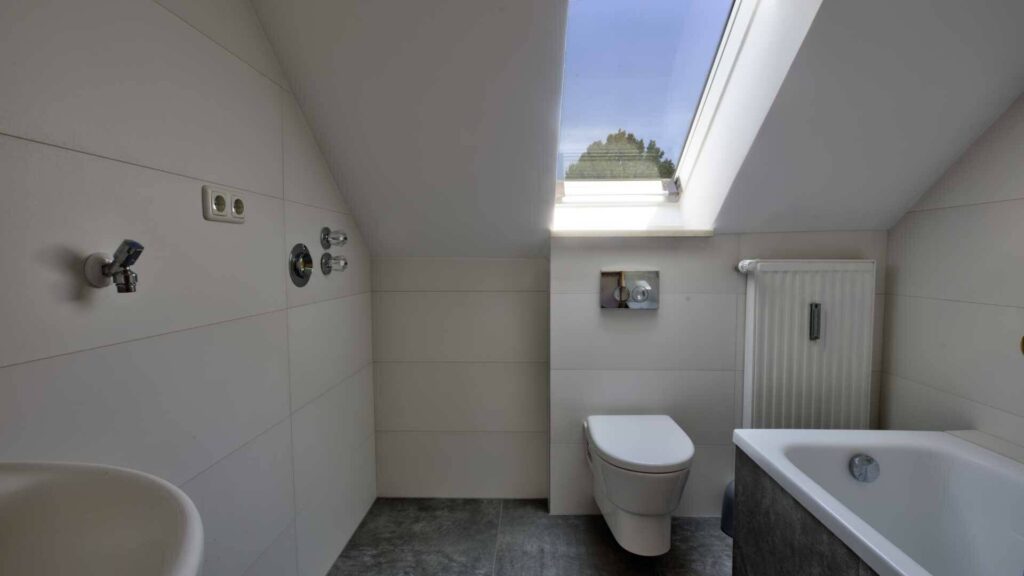 Badezimmer des Hauses in Lochhausen mit Dachfenster, Badewanne, WC und dunklem Boden