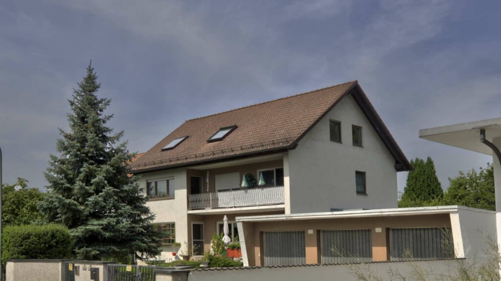 Weißes Wohnhaus in Lochhausen mit rotem Satteldach, Balkon und großem Nadelbaum davor