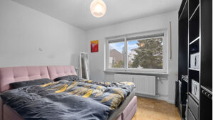 Schlafzimmer der Wohnung in München-Lochhausen mit rosa Polsterbett und schwarzem Schrank