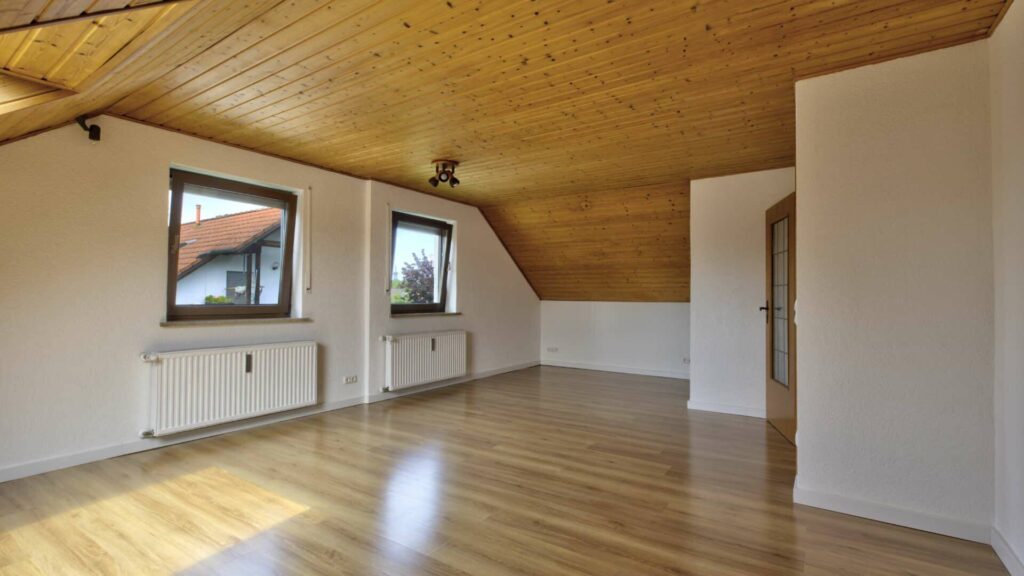 Leeres Wohnzimmer des Hauses in Lochhausen mit Holzdecke, zwei Fenstern und glänzendem Boden