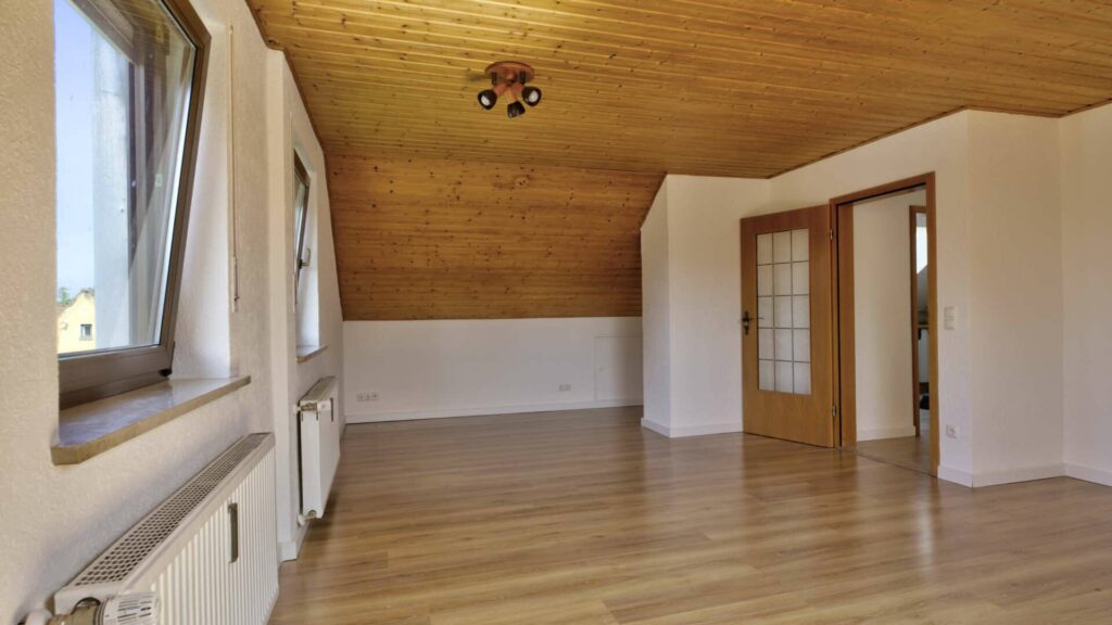 Leeres Wohnzimmer des Hauses in Lochhausen mit Holzdecke, Fenster und hellem Parkettboden