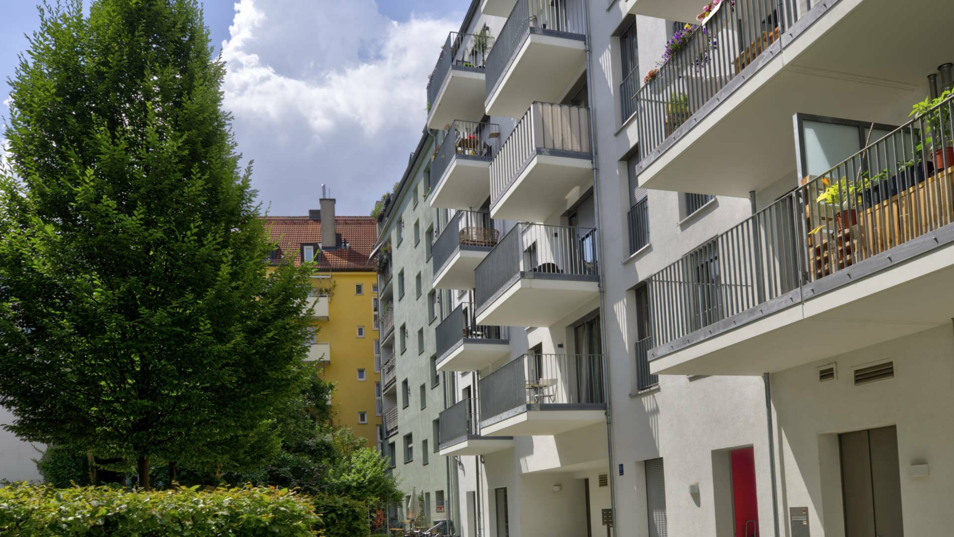 Modern residential building with wrap-around balconies and a tree in Ludwigsvorstadt, Munich