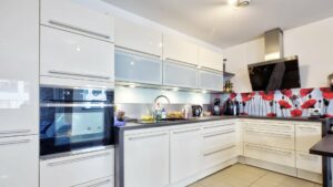 White fitted kitchen with red and white wall motif and dark countertop in Ludwigsvorstadt