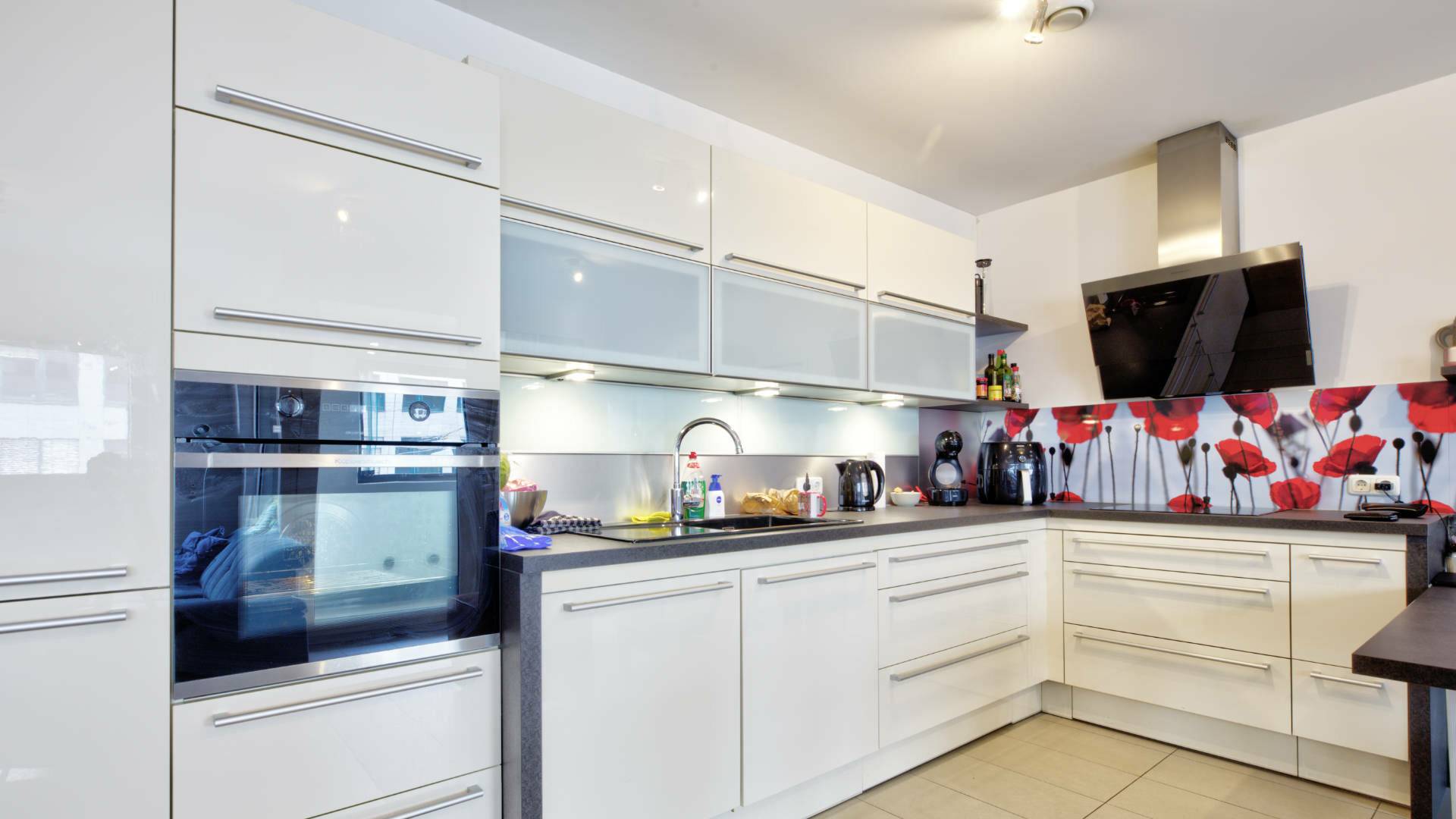 White fitted kitchen with red and white wall motif and dark countertop in Ludwigsvorstadt