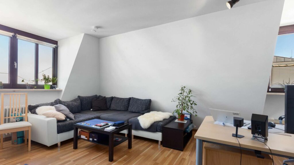 Wohnzimmer der Wohnung in der Ludwigsvorstadt in München mit dunkler Eckcouch unter der Dachschräge