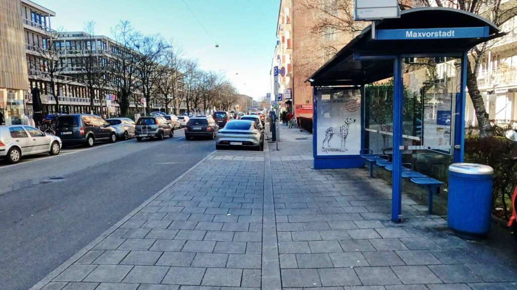 Street view with bus stop and parked cars in front of the retail space in Munich-Maxvorstadt