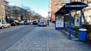 Street view with bus stop and parked cars in front of the retail space in Munich-Maxvorstadt