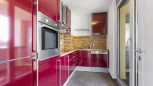 Einbauküche mit glänzend roten Fronten, Einbaubackofen und Balkonzugang in einer Wohnung in München-Milbertshofen