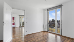 Unmöbliertes Zimmer mit Parkettboden, Balkontür und Durchblick zu weiterem Raum in einer Wohnung in München-Milbertshofen