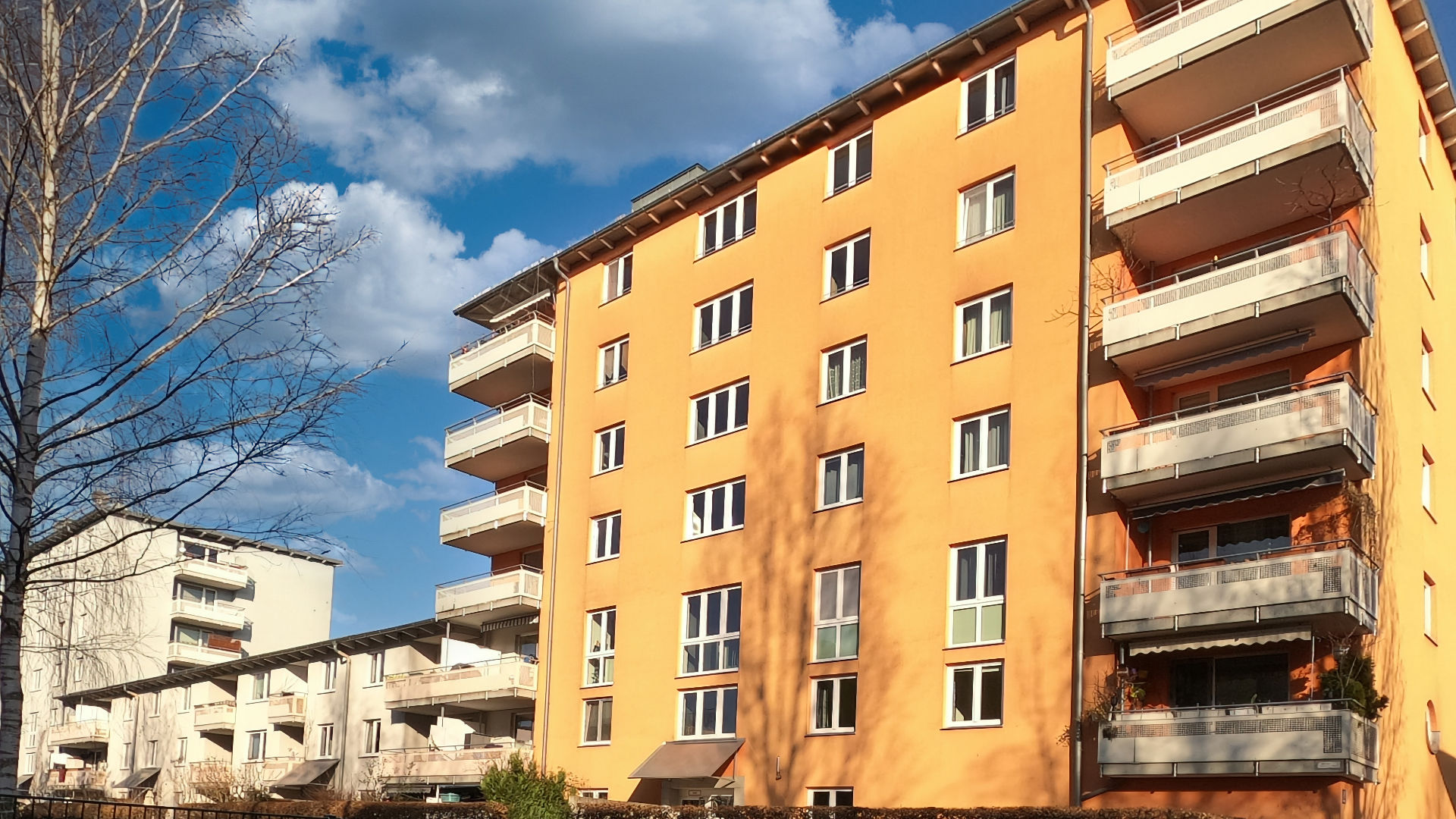 Ockerfarbenes mehrstöckiges Wohnhaus mit umlaufenden Balkonen im Stadtteil Milbertshofen in München