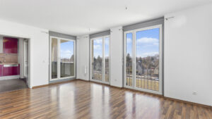 Unfurnished living space with balcony doors and a view of the red kitchen area in an apartment in Munich-Milbertshofen